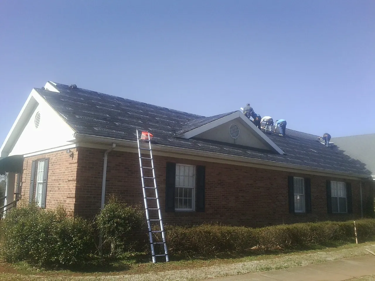 Crew tearing shingles off a brick ranch roof with a ladder set — Metal Roof Repair work by our crew in Berkshire