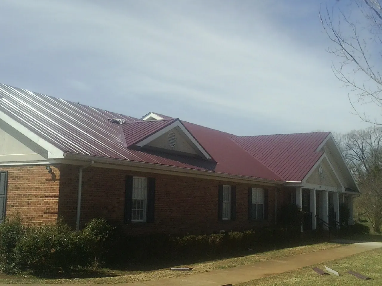 Red metal roof with gabled entries on a long brick building, from a Hail Damage Roof Repair job in Berkshire