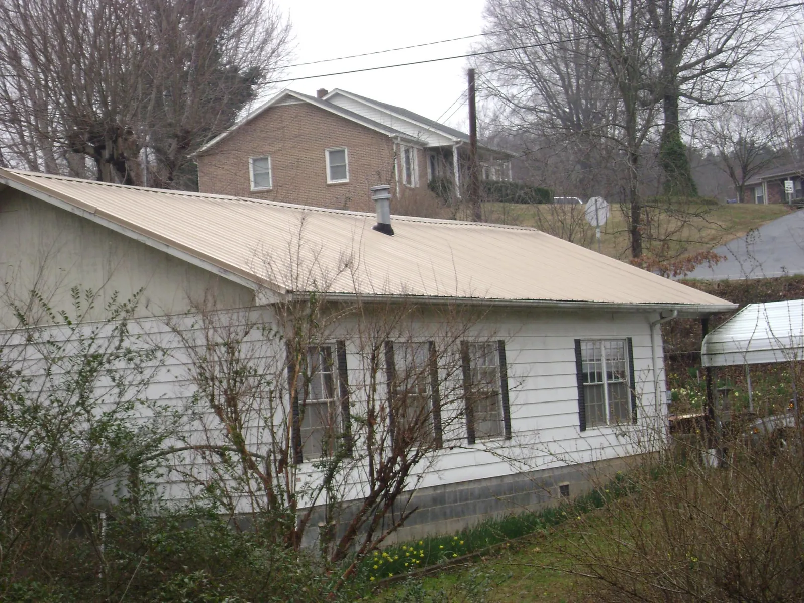 Tan metal roof on a white sided house set into a hillside — Commercial Roofing by Roofing Brothers in Berkshire